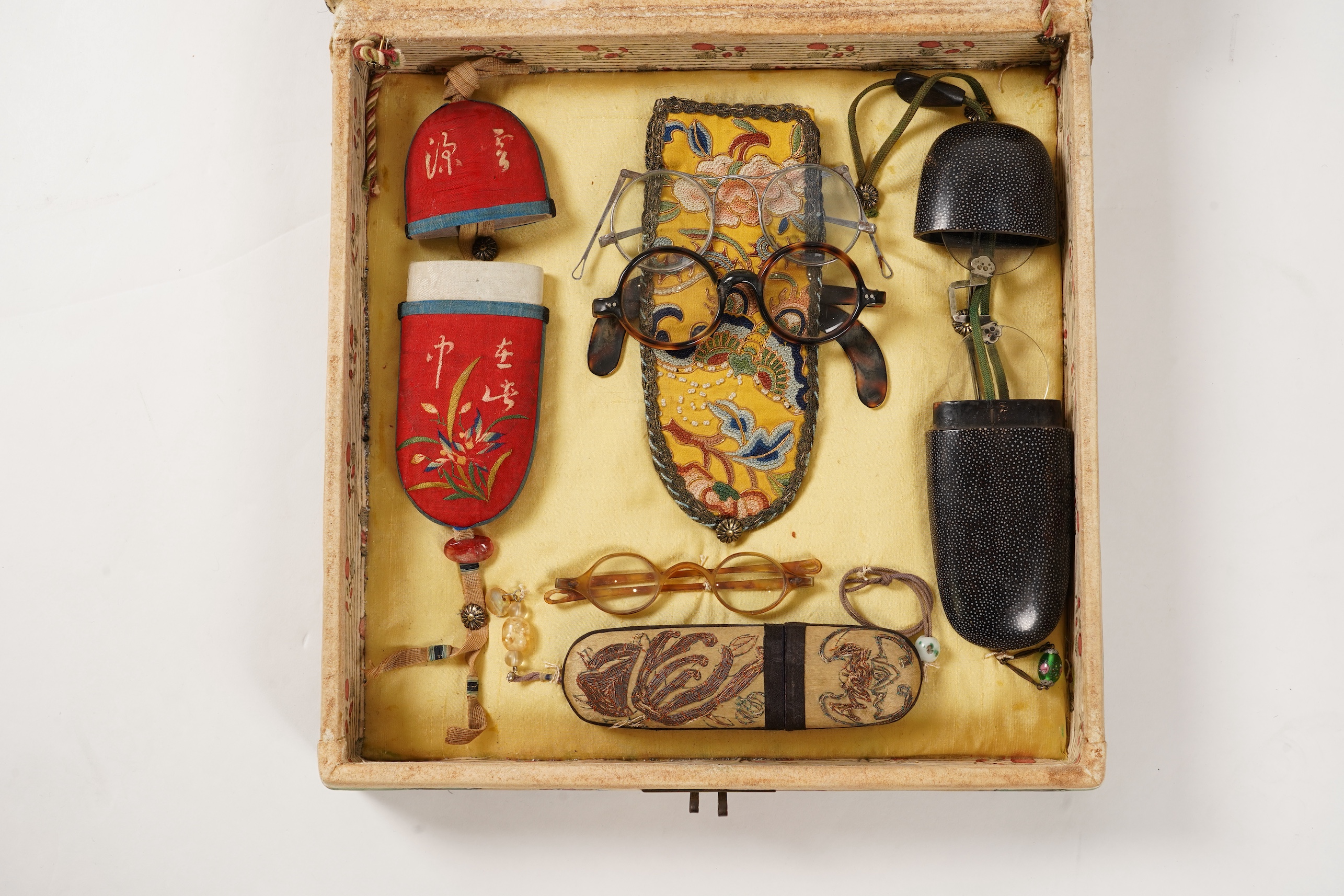A collection of 19th/20th century Chinese embroidered silk spectacle cases and various spectacles, Box 33cm square